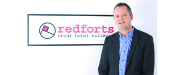 Jan Korstanje, socio fundador de Redforts, de pie con confianza frente al logo de Redforts Oscar Hotel Software.
