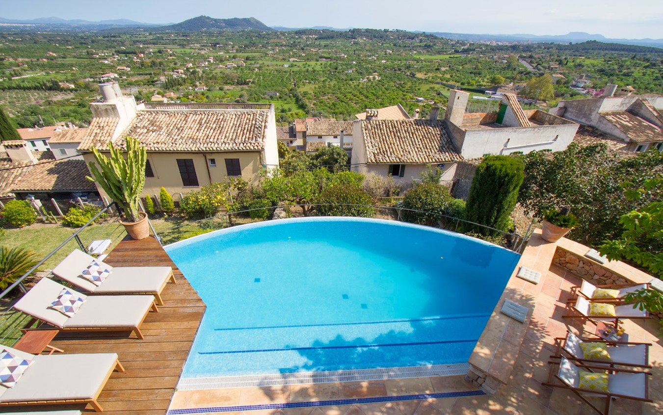 Hotel Can Cota's inviting pool with deck chairs overlooking the lush landscape of Selva, Mallorca, managed by Isabel Munar using Redforts software.