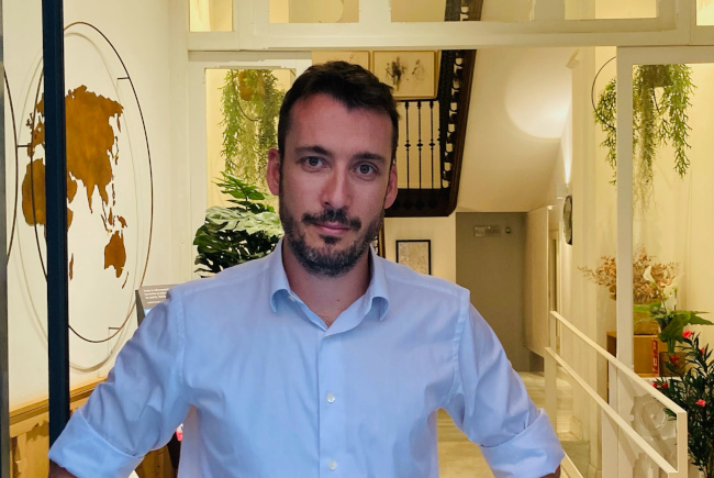 Cedric Sachs, standing confidently in the lobby of Plaza Mayor Suites & Apartments in Madrid, with a world map in the background, highlighting his journey in the hospitality industry supported by Redforts software.